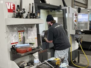 Employee loading a CNC machine with a metal cylinder.