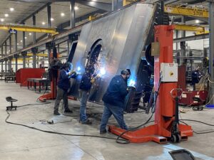 Three workers in protective gear are welding a large metal structure.