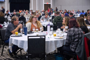 Attendees seated at round tables during a conference event.