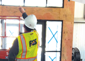 Worker in safety gear inspecting a window frame indoors.