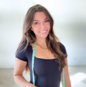 Smiling woman in black shirt with measuring tape around neck.