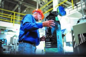 Worker in orange hard hat inspecting a bag on production line.